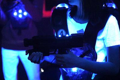 Obrázek dvou hráčů laser game. Vesty svítí modře. Hráčka v popředí míří zbraní.