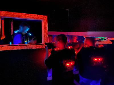 Dva hráči laser game mířící na sebe zbraní skrz okno ve zdi